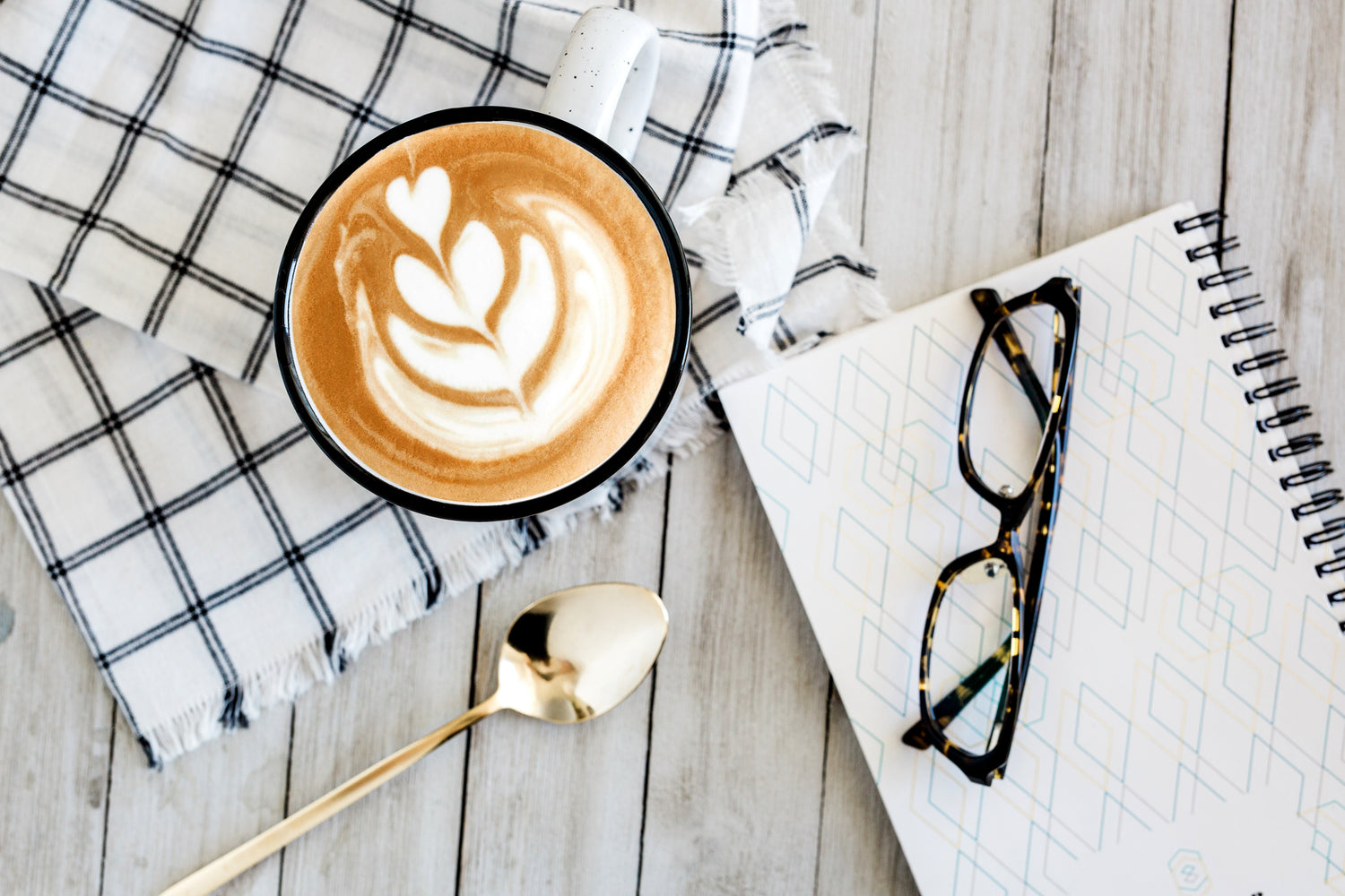 latte-art-on-rustic-table-next-to-notebook-and-glasses