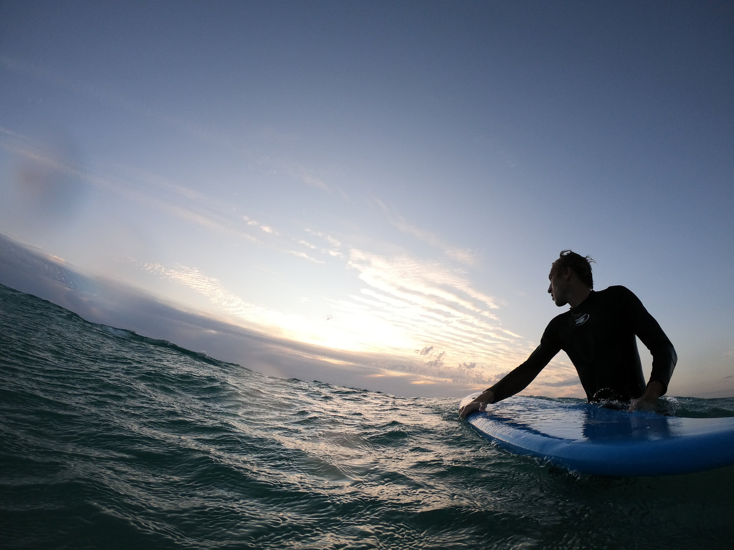 on the sea surfing on a surfboard a single male sits on it in the sunset