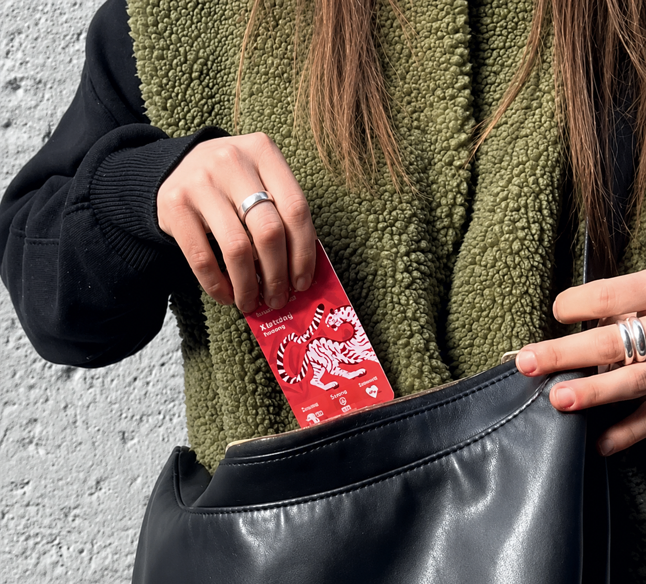 Person holding a red card with a tiger design and a black leather bag against a gray background