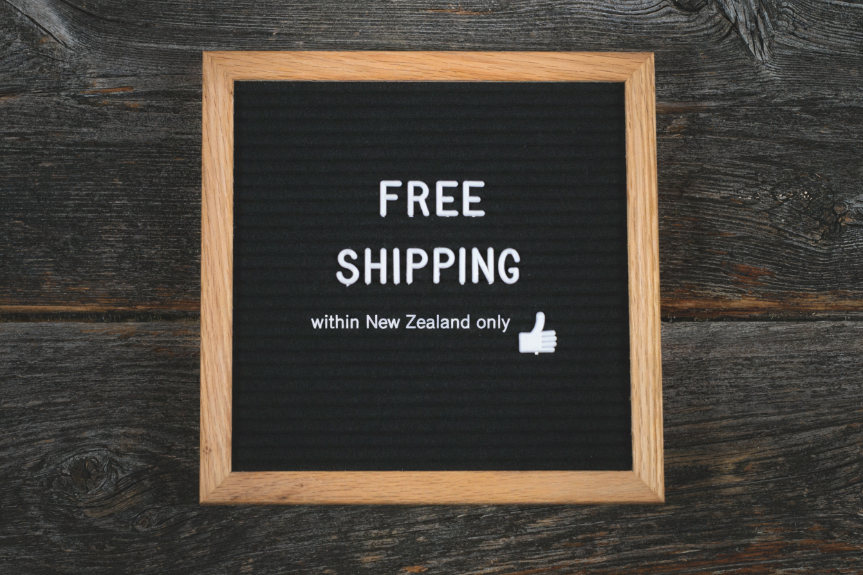 Black letter board with 'Free Shipping within New Zealand only' text on a wooden surface