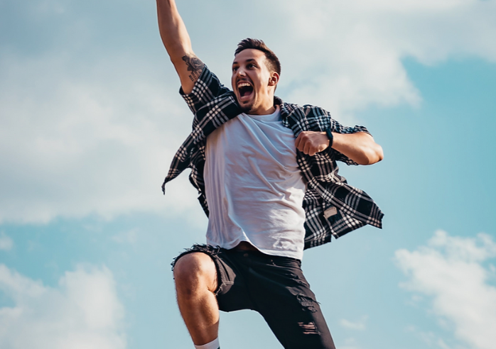 male jumping in air with a happy face and hands in the air